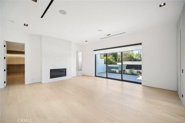 unfurnished living room with light wood-style floors and a glass covered fireplace