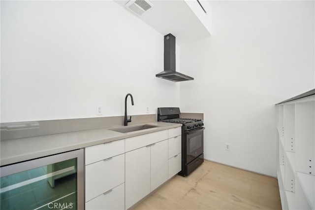 kitchen with beverage cooler, light countertops, black gas stove, wall chimney range hood, and white cabinetry