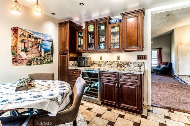 kitchen featuring light stone countertops, beverage cooler, light colored carpet, and a textured ceiling