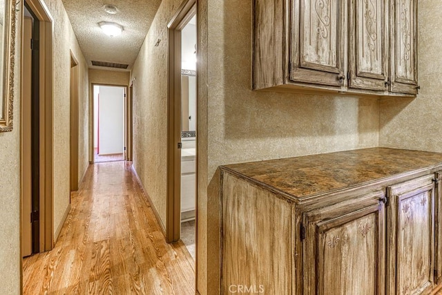 corridor featuring a textured ceiling and light hardwood / wood-style flooring