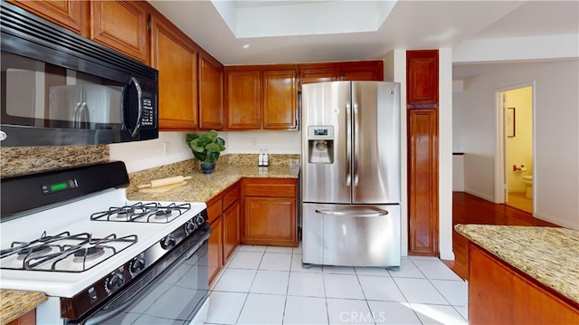 kitchen with light stone counters, light tile patterned floors, stainless steel refrigerator with ice dispenser, and white range with gas cooktop