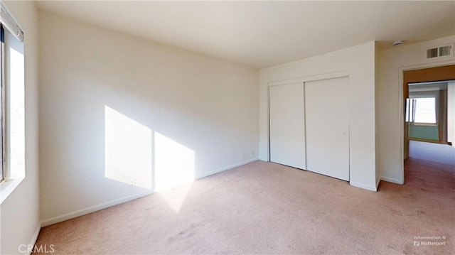 unfurnished bedroom with multiple windows, light carpet, and a closet