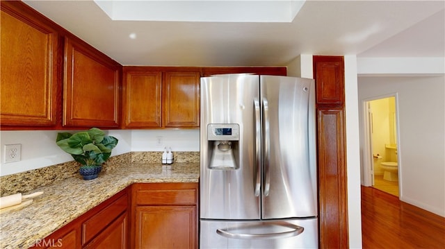 kitchen with stainless steel fridge, light stone counters, and hardwood / wood-style floors