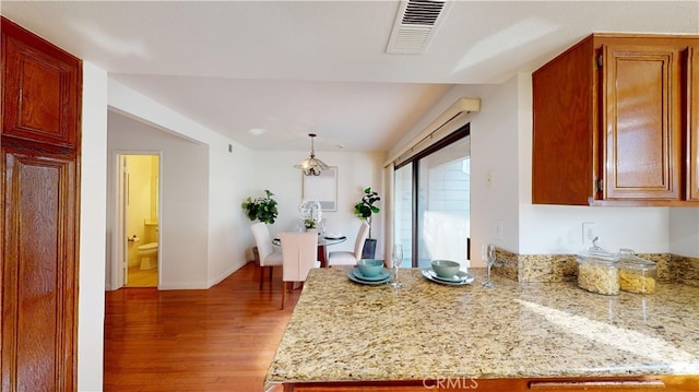 kitchen with light stone counters, light hardwood / wood-style flooring, and decorative light fixtures