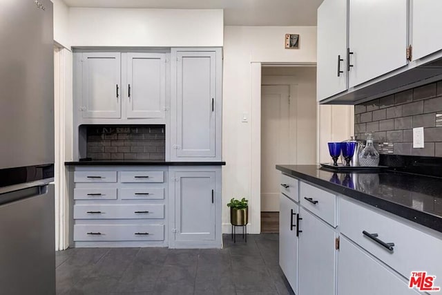 kitchen featuring tasteful backsplash, white cabinetry, stainless steel refrigerator, and dark stone counters