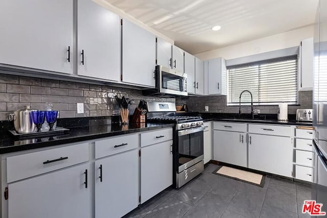 kitchen with sink, white cabinetry, appliances with stainless steel finishes, dark tile patterned flooring, and decorative backsplash