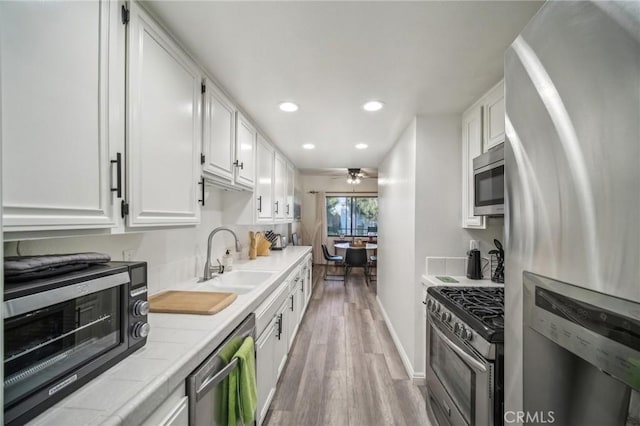 kitchen with tile counters, white cabinets, appliances with stainless steel finishes, and sink