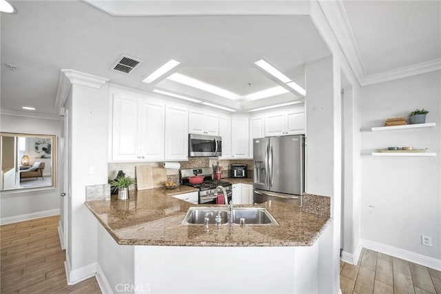 kitchen with kitchen peninsula, stainless steel appliances, sink, stone counters, and white cabinetry