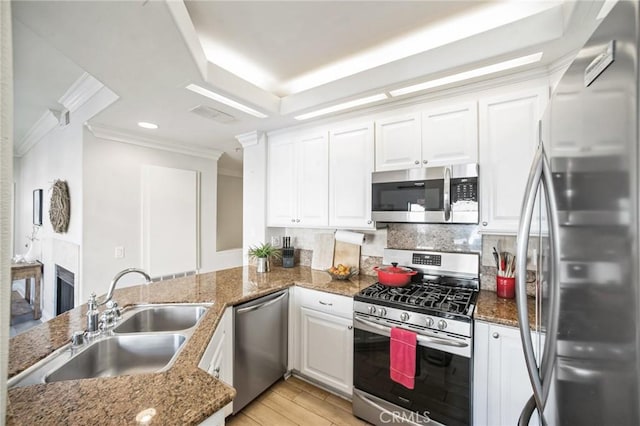 kitchen featuring sink, stainless steel appliances, kitchen peninsula, dark stone counters, and white cabinets