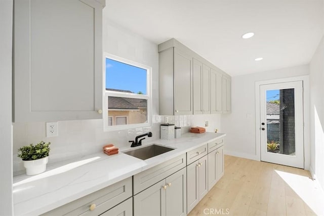 kitchen with light hardwood / wood-style flooring, light stone counters, sink, and tasteful backsplash