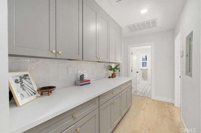 kitchen with gray cabinets, light wood-type flooring, backsplash, and electric panel