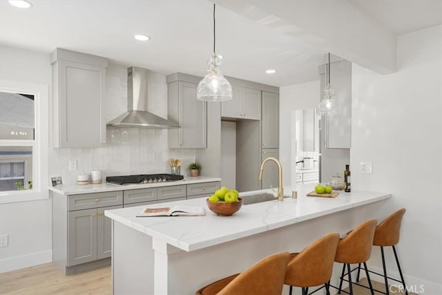 kitchen with stainless steel gas stovetop, backsplash, sink, wall chimney exhaust hood, and kitchen peninsula