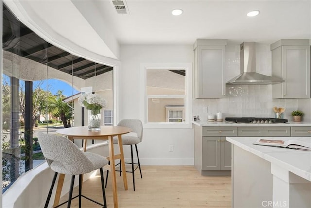 kitchen featuring decorative backsplash, stainless steel gas cooktop, gray cabinetry, and wall chimney range hood