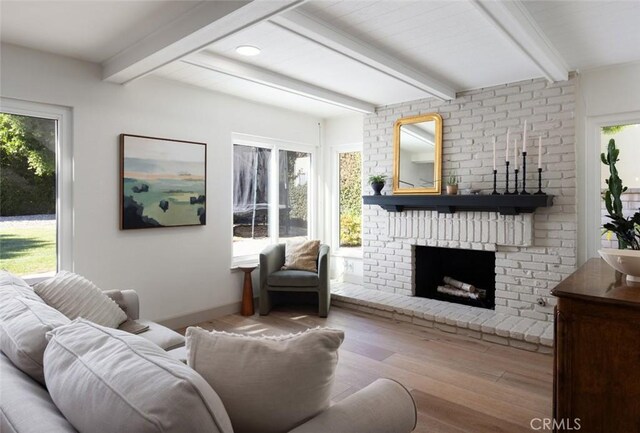 living room with hardwood / wood-style flooring, a wealth of natural light, a brick fireplace, and beamed ceiling