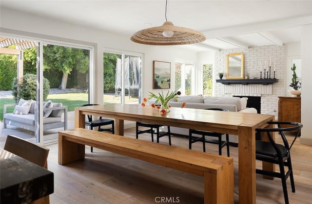 dining area with a brick fireplace, light hardwood / wood-style flooring, and beamed ceiling