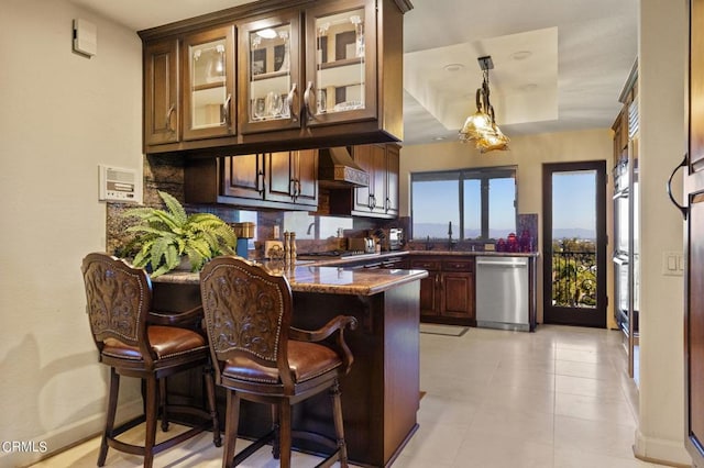 kitchen with decorative backsplash, appliances with stainless steel finishes, wall chimney exhaust hood, a tray ceiling, and dark stone countertops