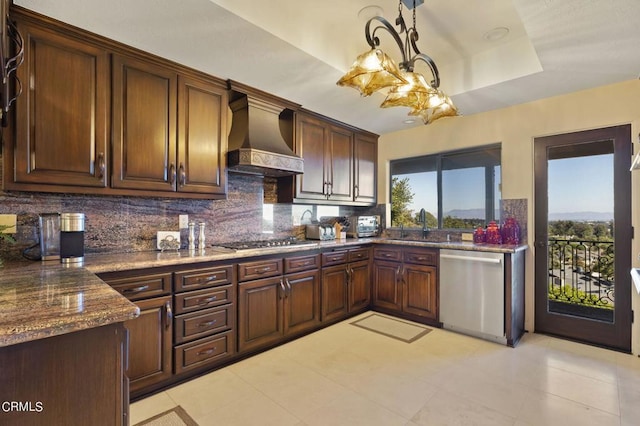 kitchen with decorative backsplash, appliances with stainless steel finishes, premium range hood, a tray ceiling, and hanging light fixtures