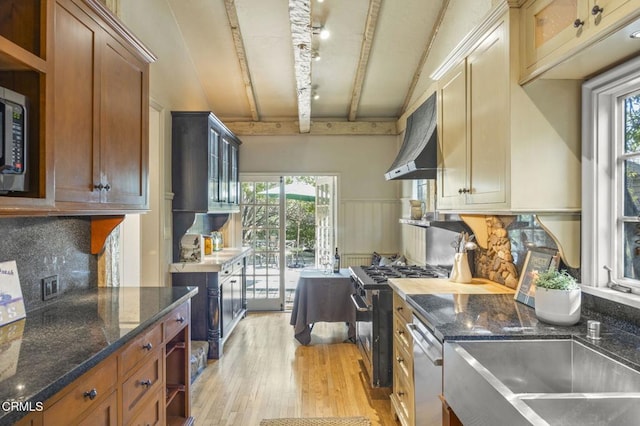 kitchen featuring beamed ceiling, dark stone countertops, light wood-type flooring, and wall chimney exhaust hood