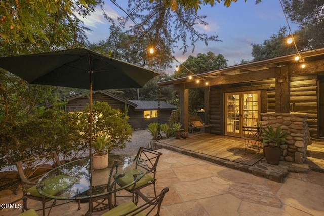 patio terrace at dusk featuring an outbuilding, a deck, and french doors