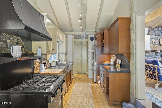 kitchen with beamed ceiling, sink, stainless steel appliances, light wood-type flooring, and wall chimney exhaust hood