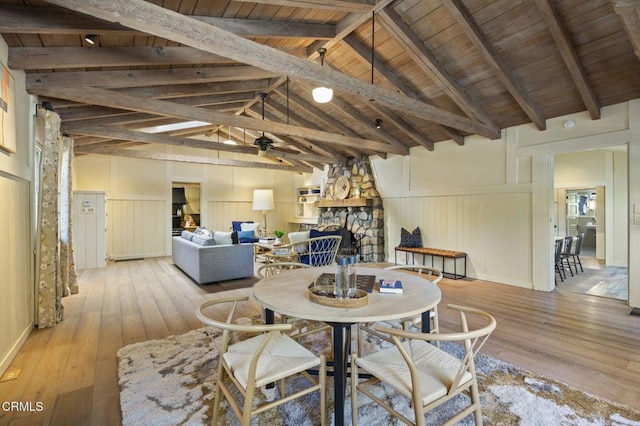 dining area featuring wooden ceiling, a stone fireplace, light hardwood / wood-style flooring, and vaulted ceiling with beams