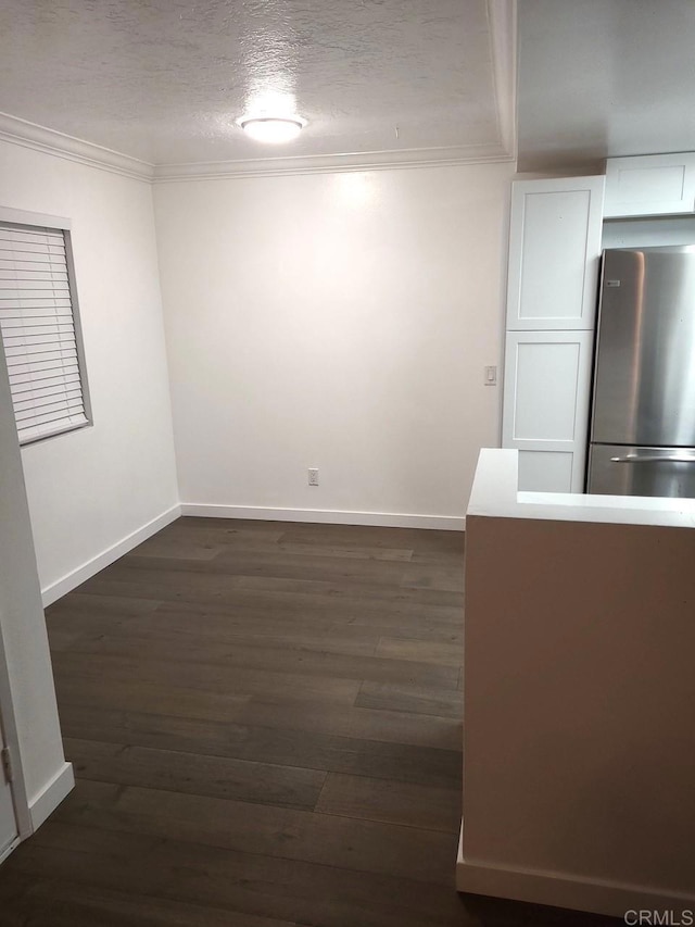 interior space featuring stainless steel refrigerator, white cabinetry, dark wood-type flooring, a textured ceiling, and ornamental molding