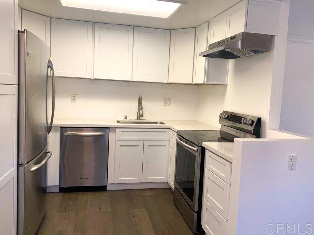 kitchen with sink, white cabinets, wall chimney range hood, and appliances with stainless steel finishes