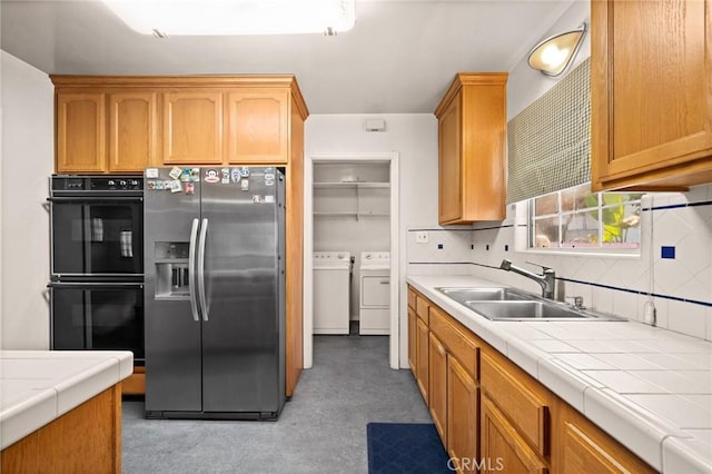 kitchen with stainless steel refrigerator with ice dispenser, black double oven, sink, washer and dryer, and tile counters