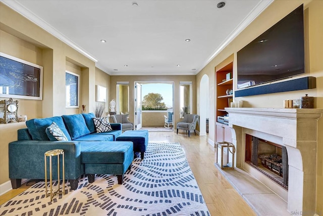 living room featuring crown molding, light wood-type flooring, a high end fireplace, and built in shelves