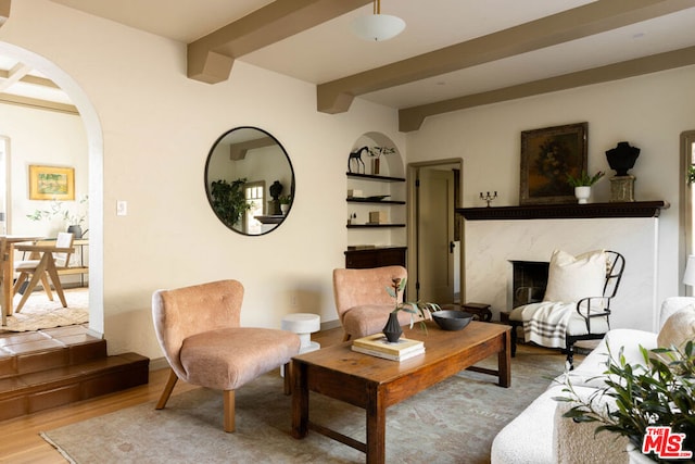 living room featuring wood-type flooring, a premium fireplace, beam ceiling, and built in features