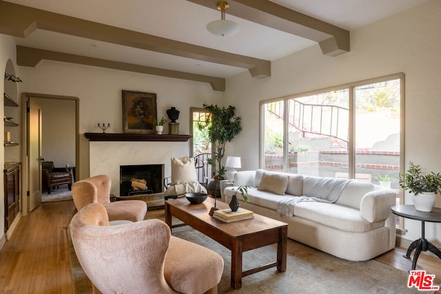 living room featuring beamed ceiling, plenty of natural light, a premium fireplace, and light hardwood / wood-style flooring