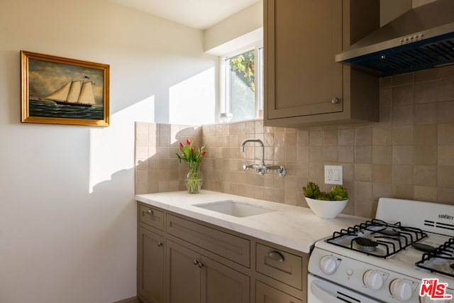 kitchen featuring tasteful backsplash, sink, light stone counters, white gas range oven, and wall chimney range hood