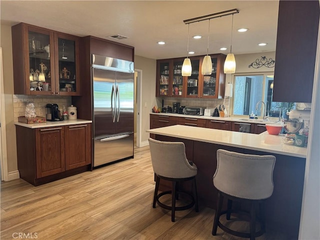 bar with light hardwood / wood-style floors, built in refrigerator, decorative backsplash, sink, and decorative light fixtures