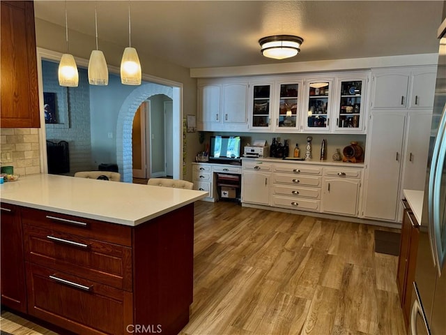 kitchen with kitchen peninsula, light hardwood / wood-style flooring, pendant lighting, decorative backsplash, and stainless steel refrigerator