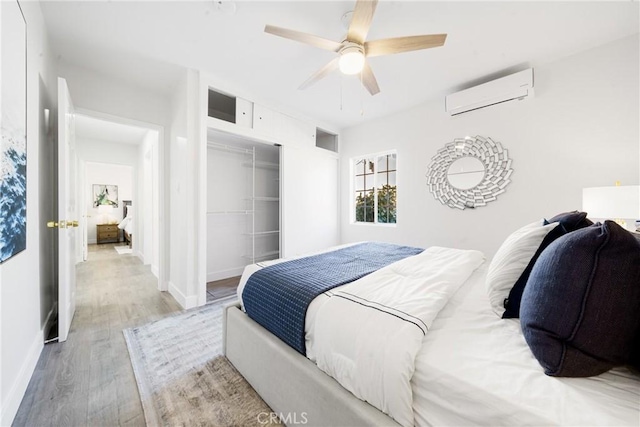 bedroom with a wall mounted AC, ceiling fan, a closet, and light wood-type flooring