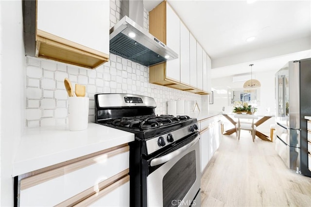 kitchen with decorative backsplash, appliances with stainless steel finishes, wall chimney exhaust hood, decorative light fixtures, and white cabinetry