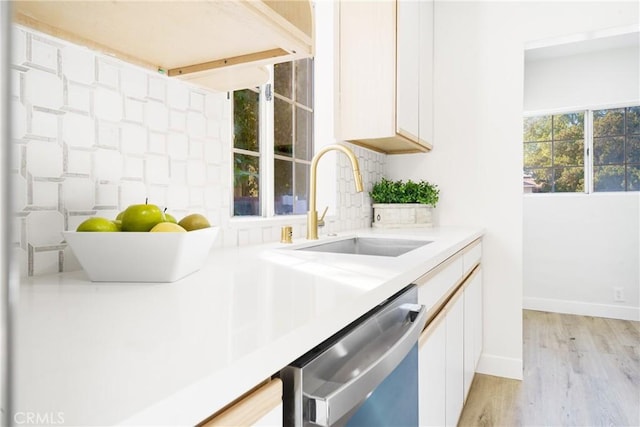 kitchen with white cabinets, sink, stainless steel dishwasher, decorative backsplash, and light wood-type flooring