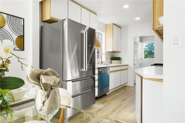 kitchen featuring white cabinetry, sink, stainless steel appliances, backsplash, and light hardwood / wood-style floors