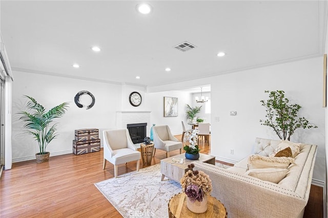 living room featuring a chandelier, crown molding, a fireplace, and hardwood / wood-style floors