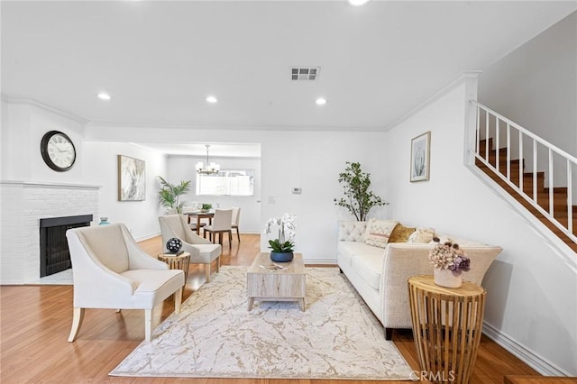 living room with an inviting chandelier, light wood-type flooring, ornamental molding, and a brick fireplace