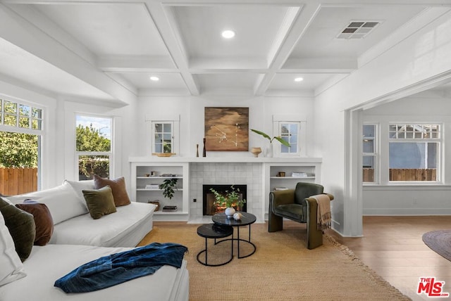 living room with beam ceiling, light hardwood / wood-style flooring, a tile fireplace, and coffered ceiling