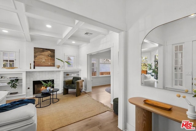 living room featuring beamed ceiling, light hardwood / wood-style floors, a fireplace, and coffered ceiling