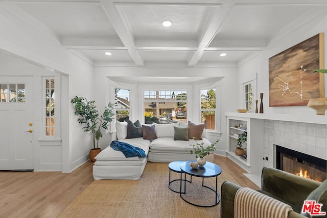 living room with a tile fireplace, coffered ceiling, light hardwood / wood-style floors, ornamental molding, and beam ceiling