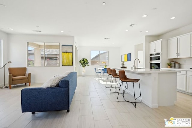 kitchen with a kitchen island with sink, a breakfast bar, white cabinets, and a healthy amount of sunlight