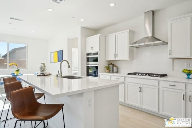 kitchen with white cabinetry, wall chimney exhaust hood, stainless steel appliances, and a kitchen island with sink