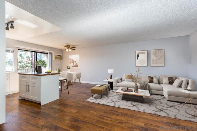 living room featuring dark hardwood / wood-style flooring, a textured ceiling, a wall unit AC, and ceiling fan