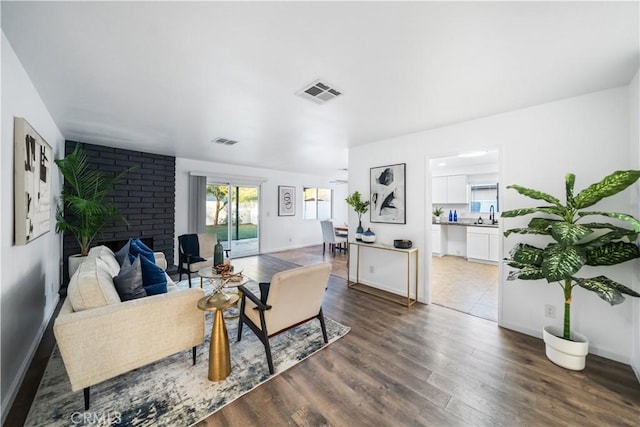 living room featuring sink, dark wood-type flooring, and a brick fireplace