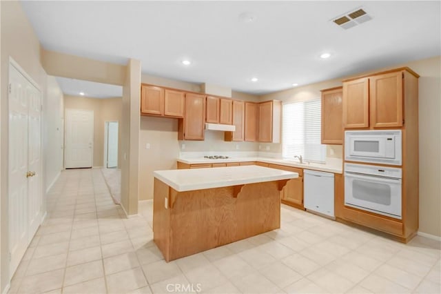 kitchen with light brown cabinets, white appliances, a center island, and sink