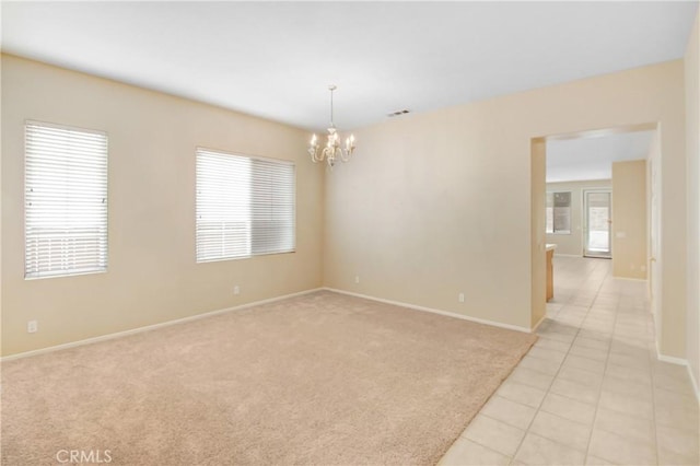 spare room featuring a notable chandelier, light tile patterned floors, and a wealth of natural light