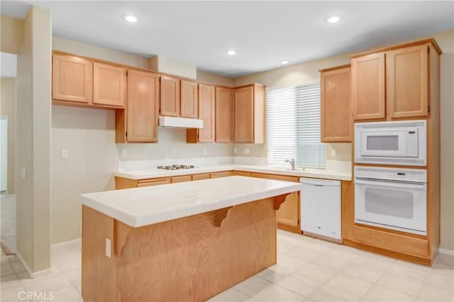 kitchen featuring a kitchen breakfast bar, a center island, white appliances, and light brown cabinetry